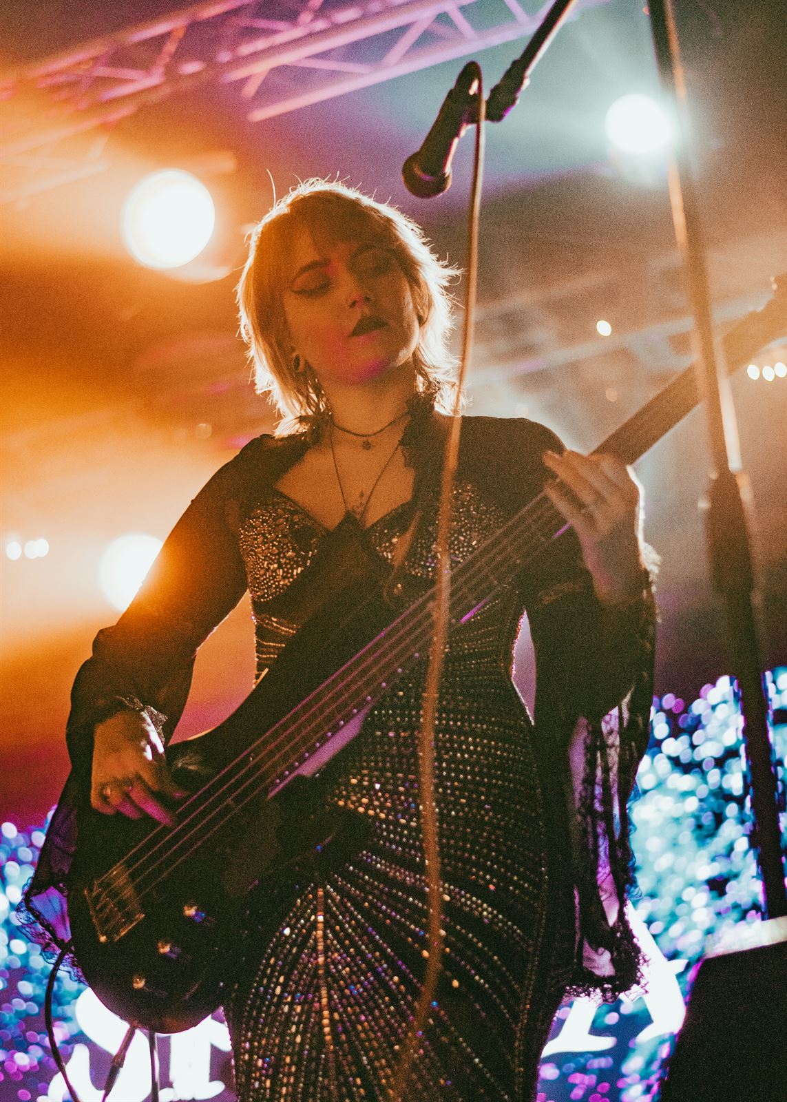 Bassist in a sequined dress under warm stage light