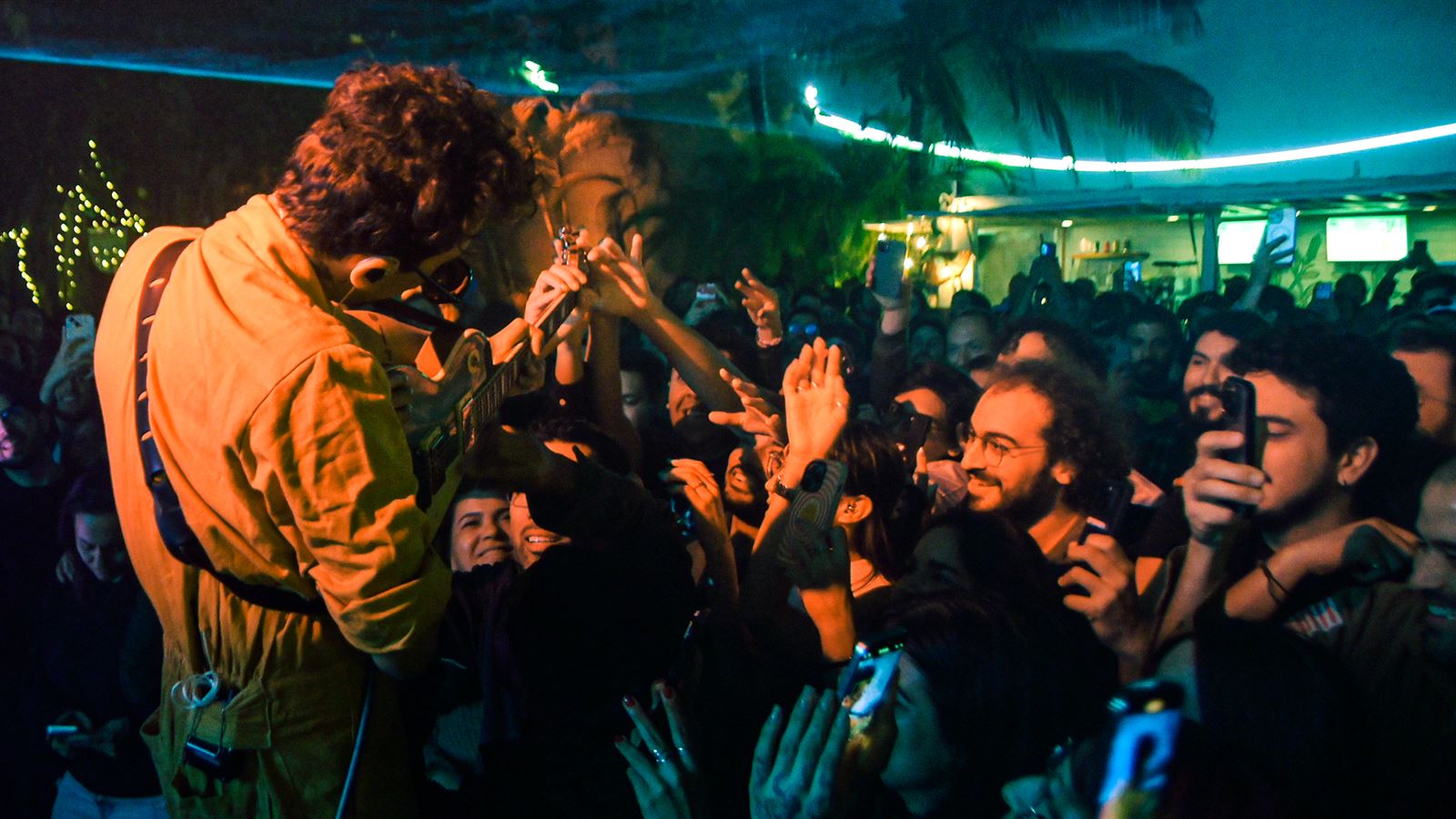 Guitarist leaning over a crowd of raised hands and phones