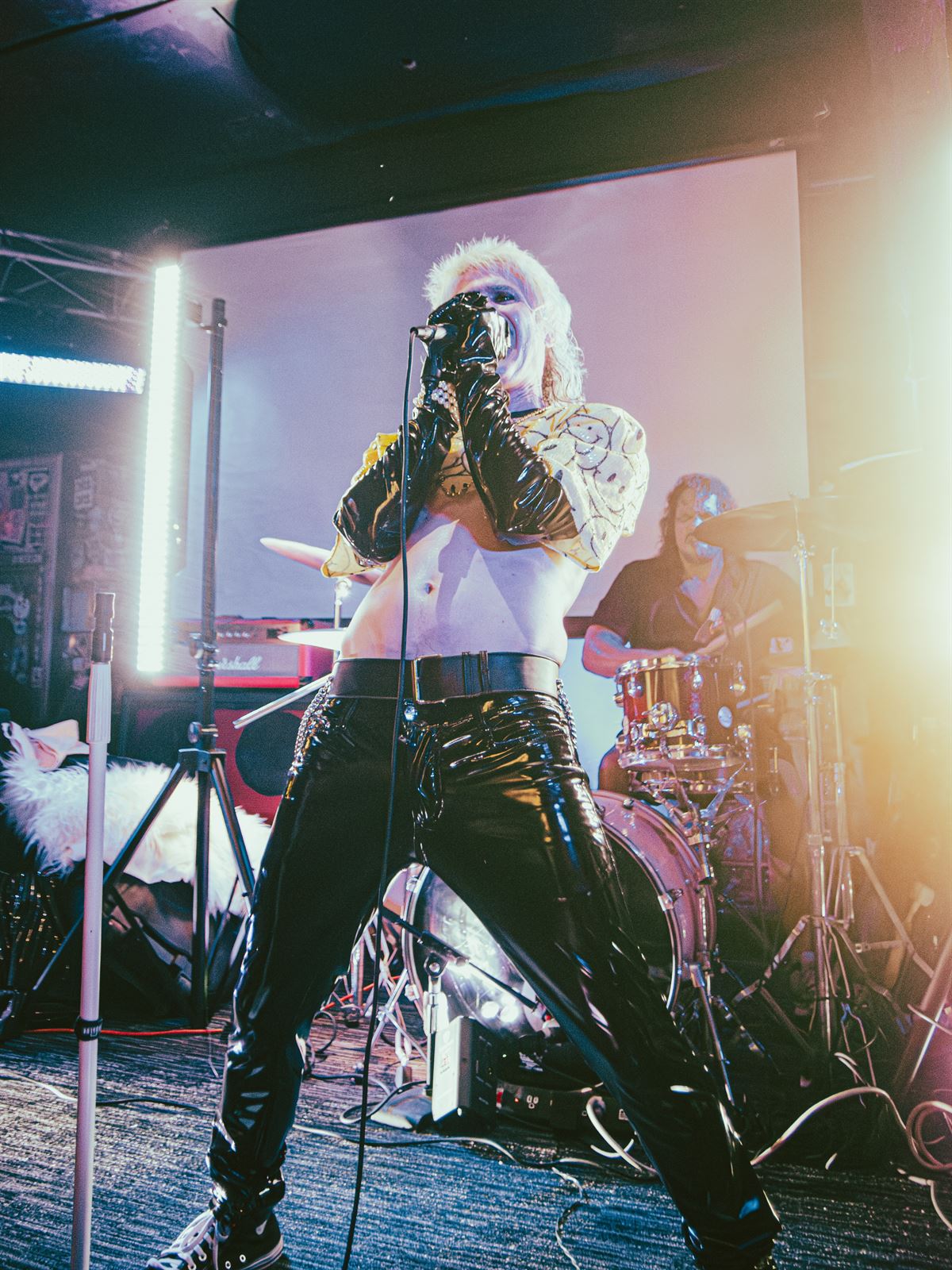 Frontman in vinyl pants gripping the mic, backlit