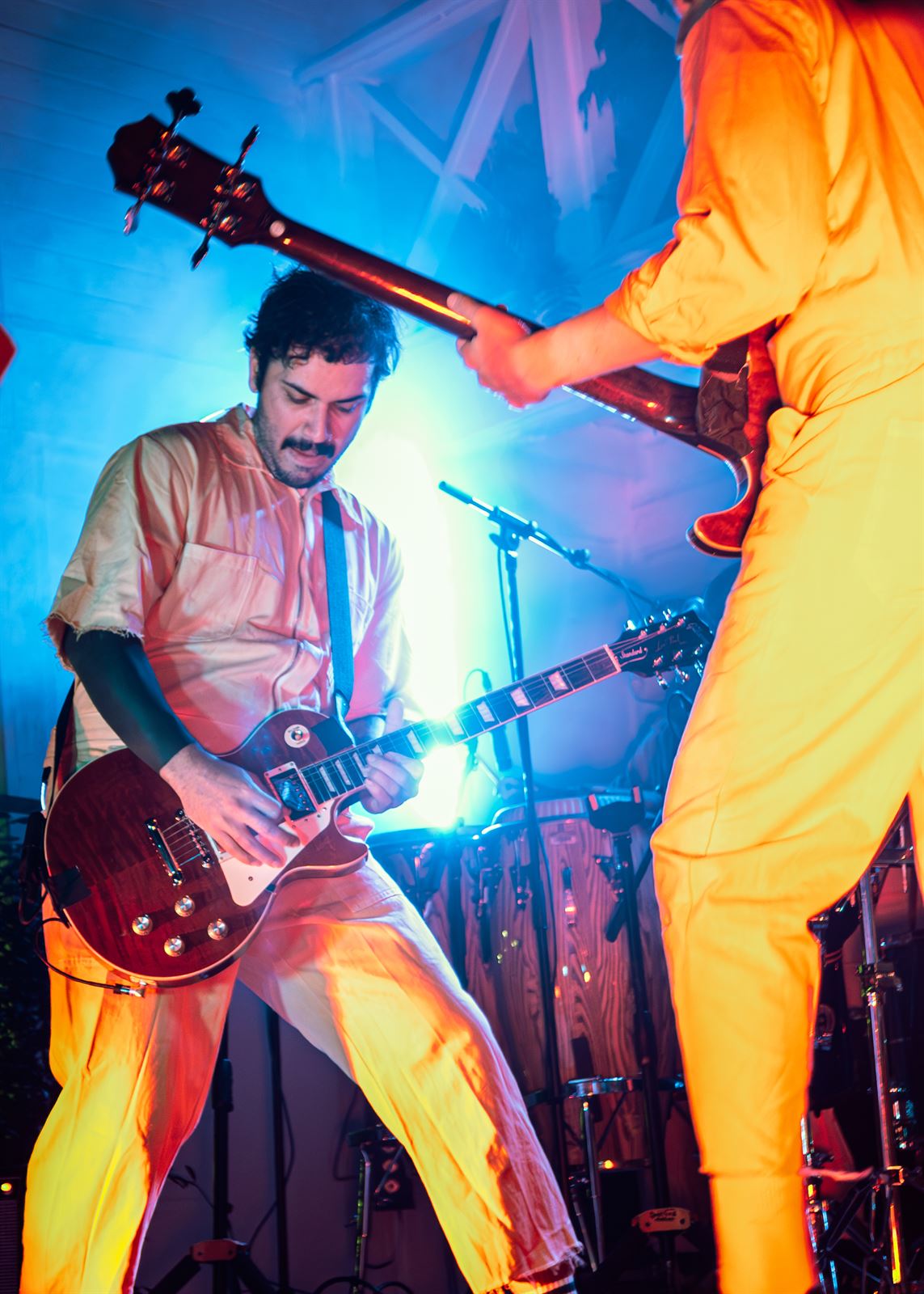 Two guitarists in orange jumpsuits under blue light