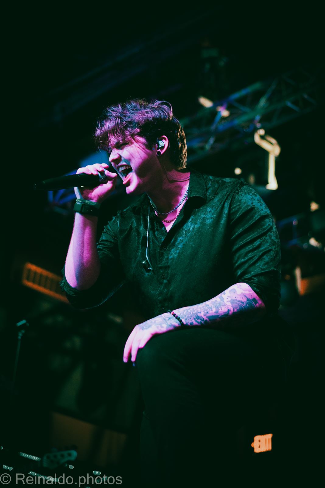 Vocalist crouched with mic in green and magenta light